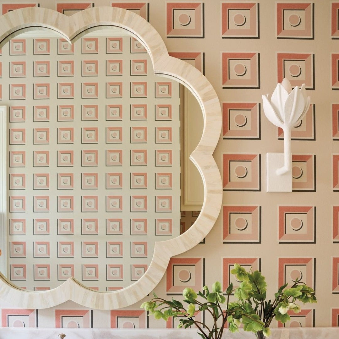 White plaster Kristy sconce on patterned pink wallpaper beside a scalloped bone-inlay mirror.