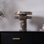 Clérachic lamp lit on the dresser with the fern branch overhead, small styled objects set on the shelf to the right.