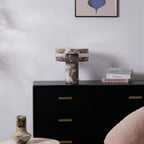 Wide bedroom view with the small Clérachic lamp on a dresser beneath a framed abstract print, a pink pouf nearby.