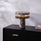 Clérachic lamp lit on the black dresser, its glow visible between the discs against the plain patterned wall.