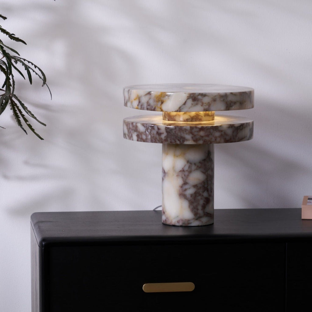 Clérachic lamp lit on the dresser with a leafy branch arching in from the left, its glow warm against the wall.