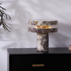 Clérachic lamp lit on the dresser with a leafy branch arching in from the left, its glow warm against the wall.