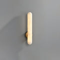 Alabaster bar wall light lit on a plain grey wall, its brass mounting disc centred on the stone.