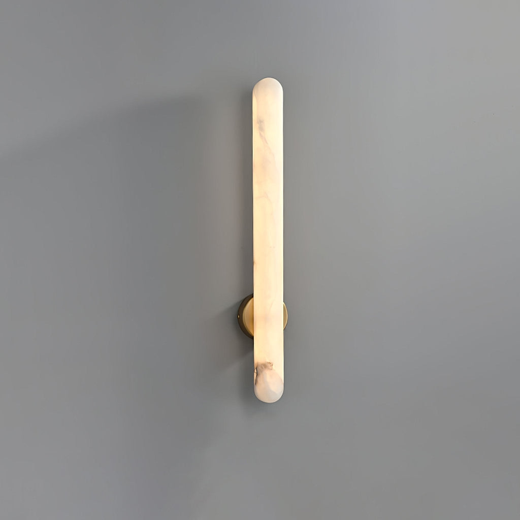 The sconce lit on grey, warm light running the full length of the rounded alabaster bar.