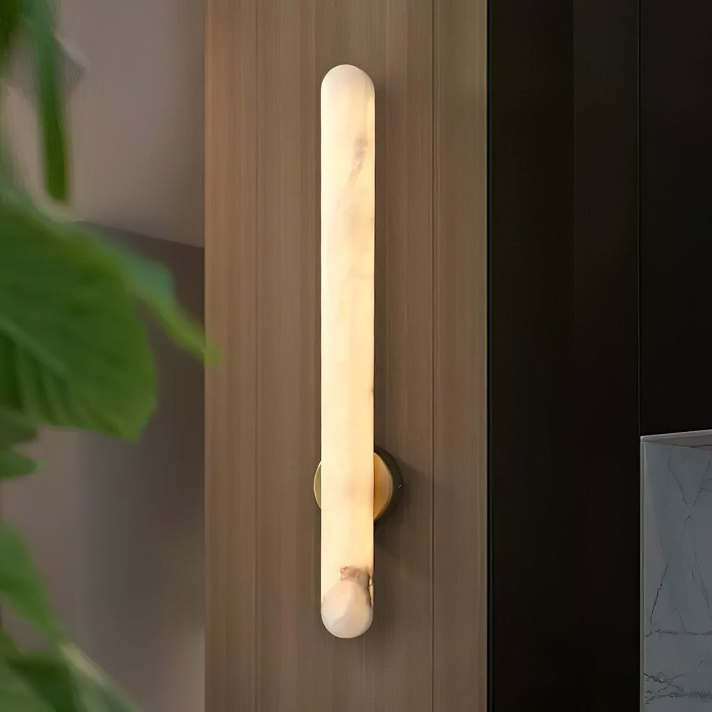 The sconce lit on a wood-panelled wall, a green leaf entering the frame at the left.