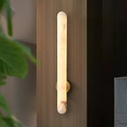 The sconce lit on a wood-panelled wall, a green leaf entering the frame at the left.