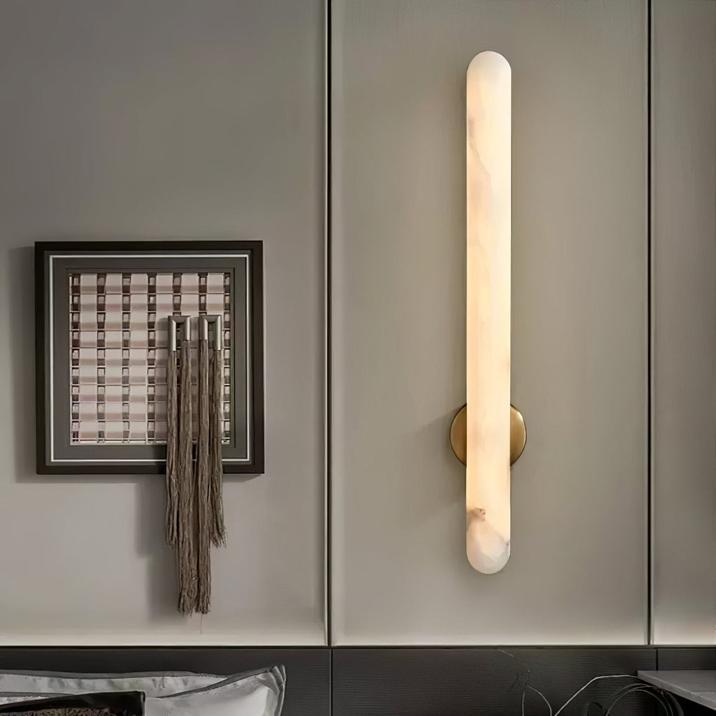 Lit on a grey panelled wall beside a framed artwork hung with woven tassels.
