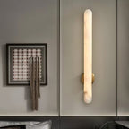 Lit on a grey panelled wall beside a framed artwork hung with woven tassels.