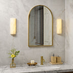 A pair of Orcarion alabaster wall lights lit either side of an arched brass mirror above a marble vanity.