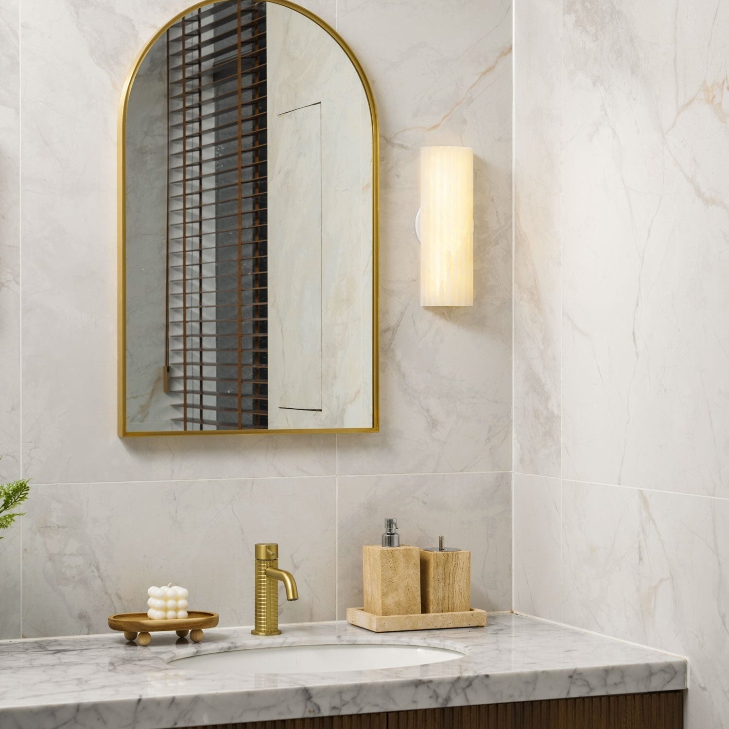 Orcarion alabaster wall light lit beside an arched brass mirror, casting warm light across marble tile.