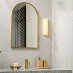Orcarion wall light lit to the right of an arched mirror, seen in a wider view of the marble bathroom.