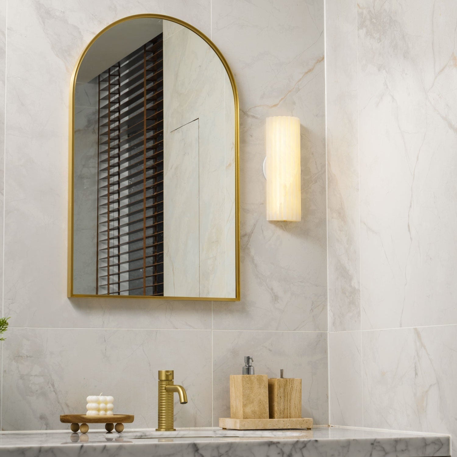 Orcarion wall light lit to the right of an arched mirror, seen in a wider view of the marble bathroom.