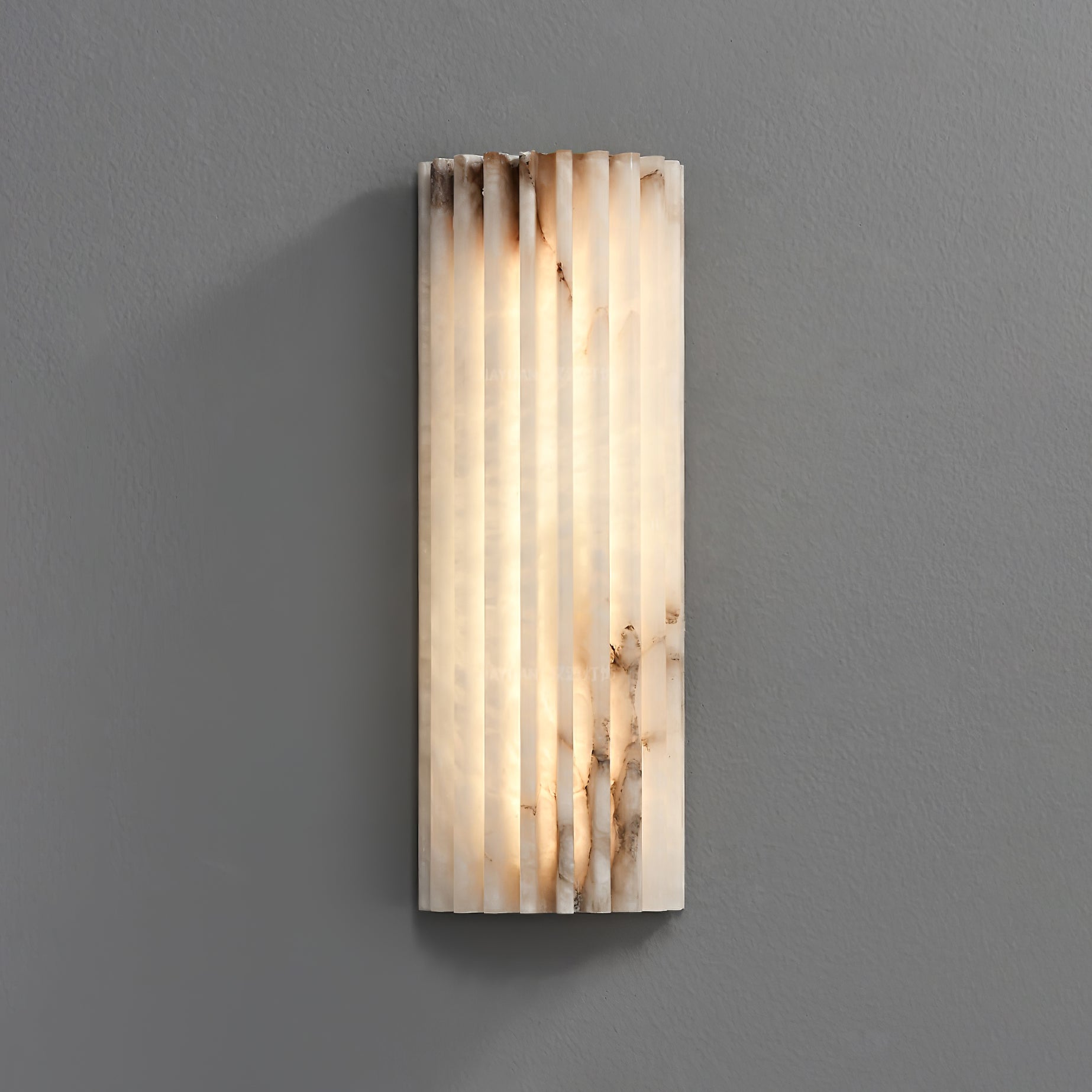 Straight-on view of the lit Orcarion alabaster wall light, showing the full width of its fluted stone face.