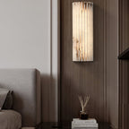 Orcarion alabaster wall light lit against a dark wood-panelled bedroom wall beside the bed.