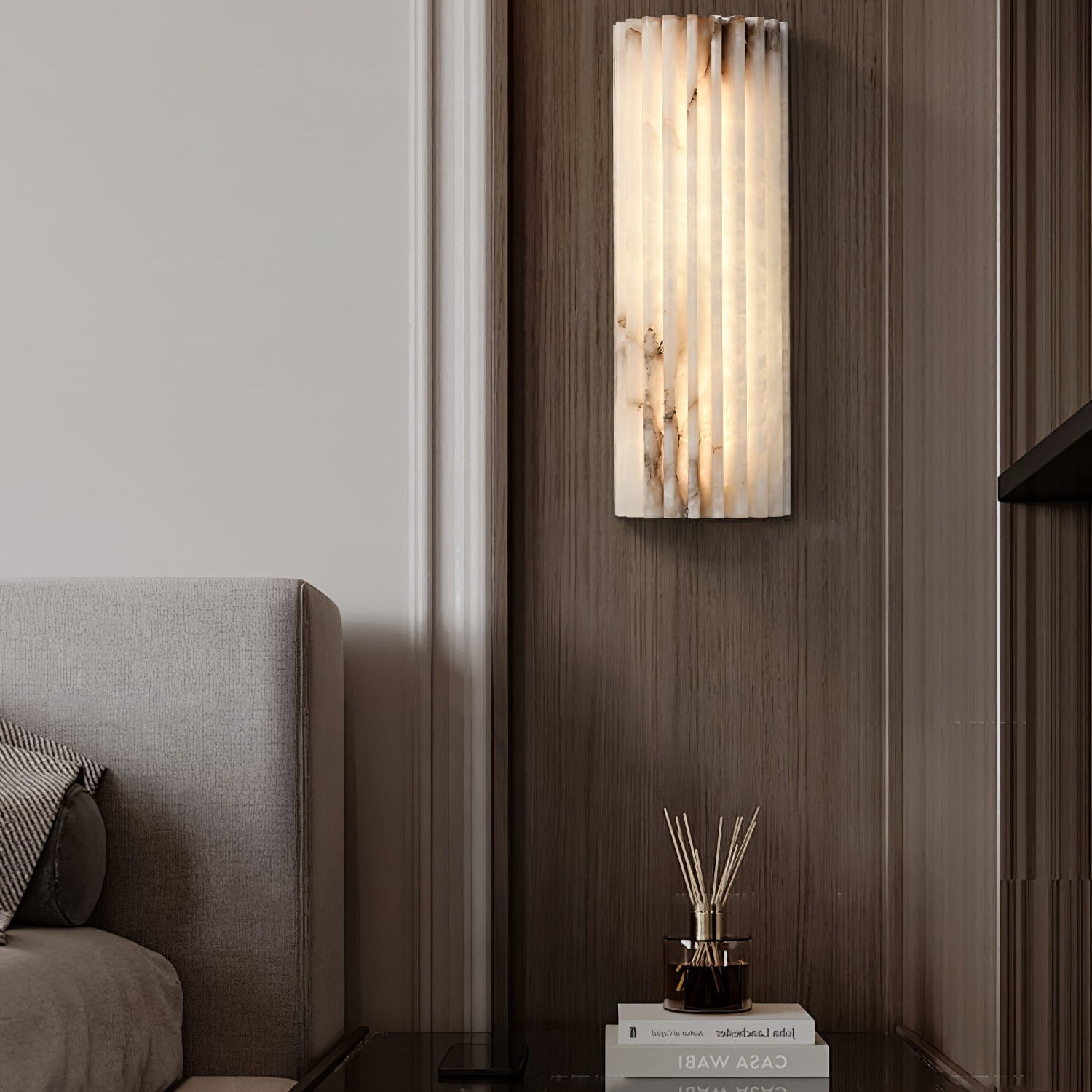Orcarion alabaster wall light lit against a dark wood-panelled bedroom wall beside the bed.