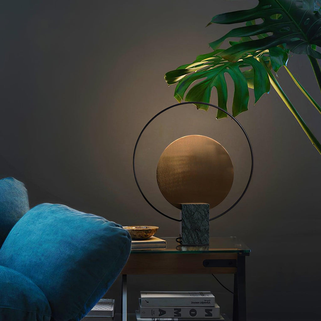 Clérachic table lamp on a side table beside a teal velvet armchair, a large monstera leaf reaching over it from above.