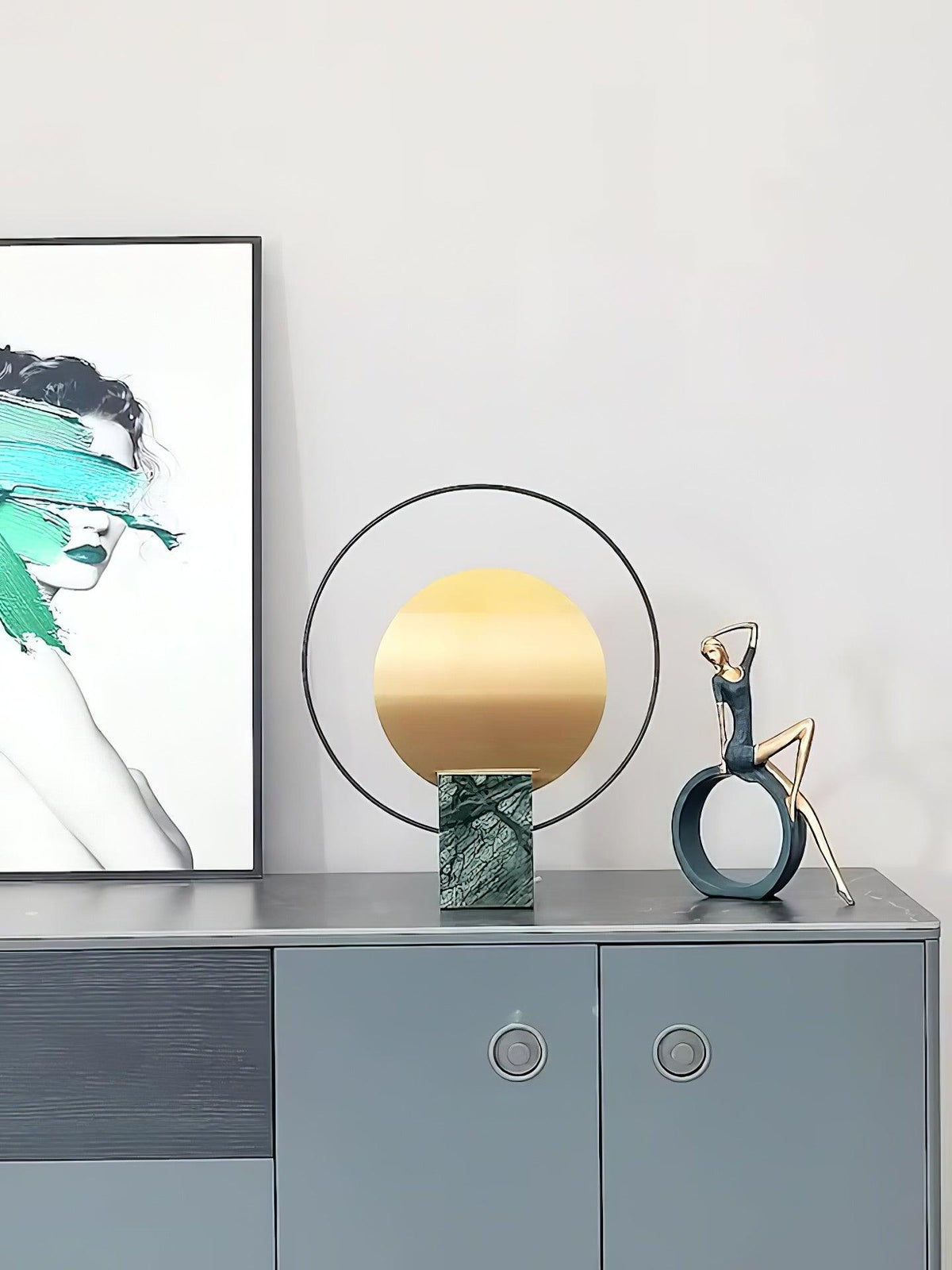 Clérachic table lamp on a blue-grey sideboard beside a framed abstract print and a small bronze figurine.
