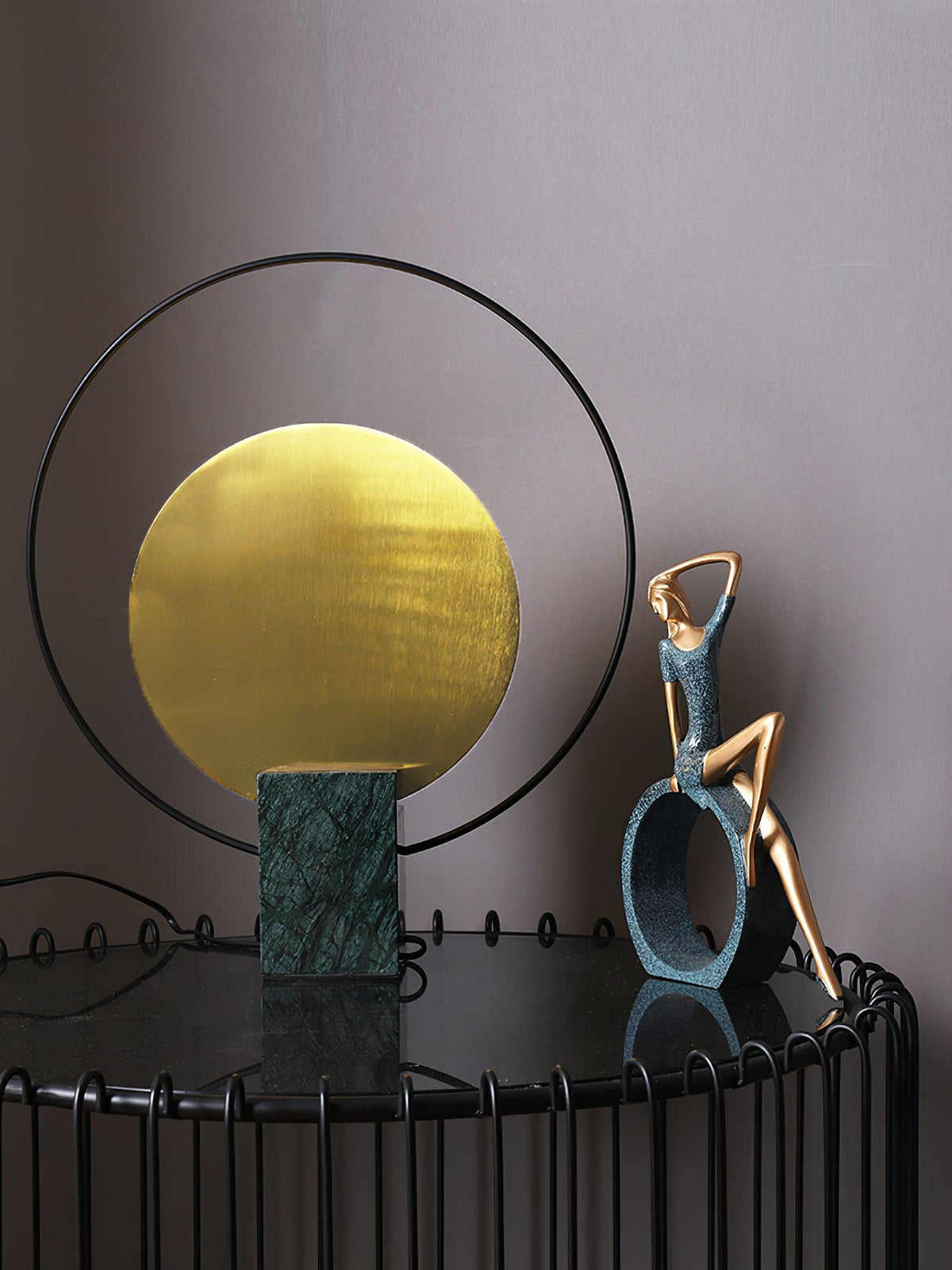 Closer crop of the Clérachic table lamp and its bronze reclining-figure companion piece on a black wire table.