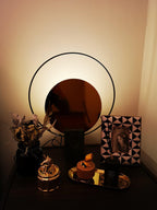 Clérachic table lamp glowing at night on a dark nightstand, dried flowers and a patterned photo frame nearby.
