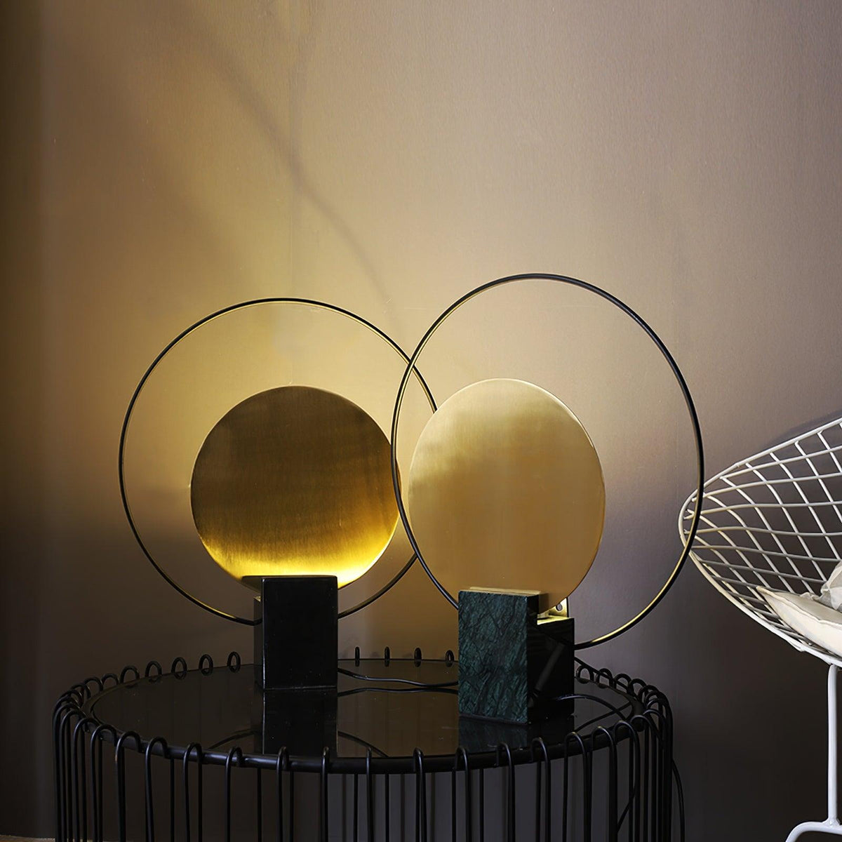 Two Clérachic table lamps, one on green marble and one on black, glowing warmly together on a wire-frame side table.