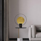 Clérachic table lamp on a slender-pedestal side table beside an armchair, sheer curtains softening the daylight behind it.