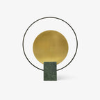 Clérachic table lamp on a plain white background, showing its brushed gold disc inside a black ring above a green marble base.