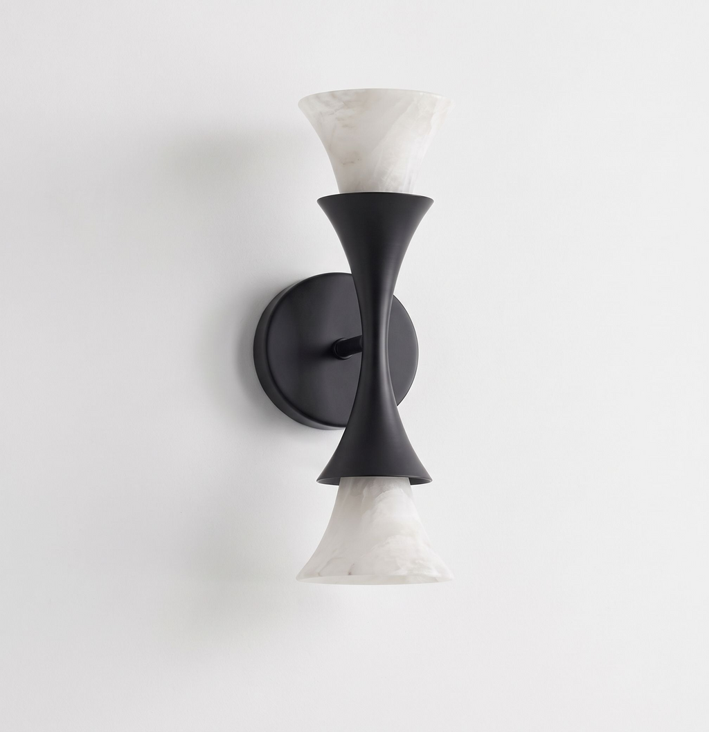 Studio product shot, this Clérachic sconce's matte black hourglass frame holds two alabaster shades against a bare white backdrop.