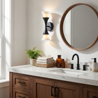 Either side of a round mirror above a dark wood vanity with ferns, these Clérachic sconces glow in matte black.