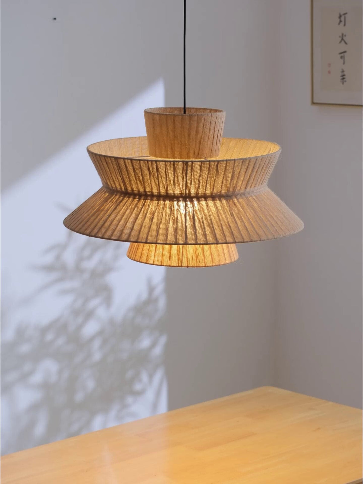 Casting a soft shadow on a plain wall, this Clérachic pendant hangs above a glossy pale wood table.