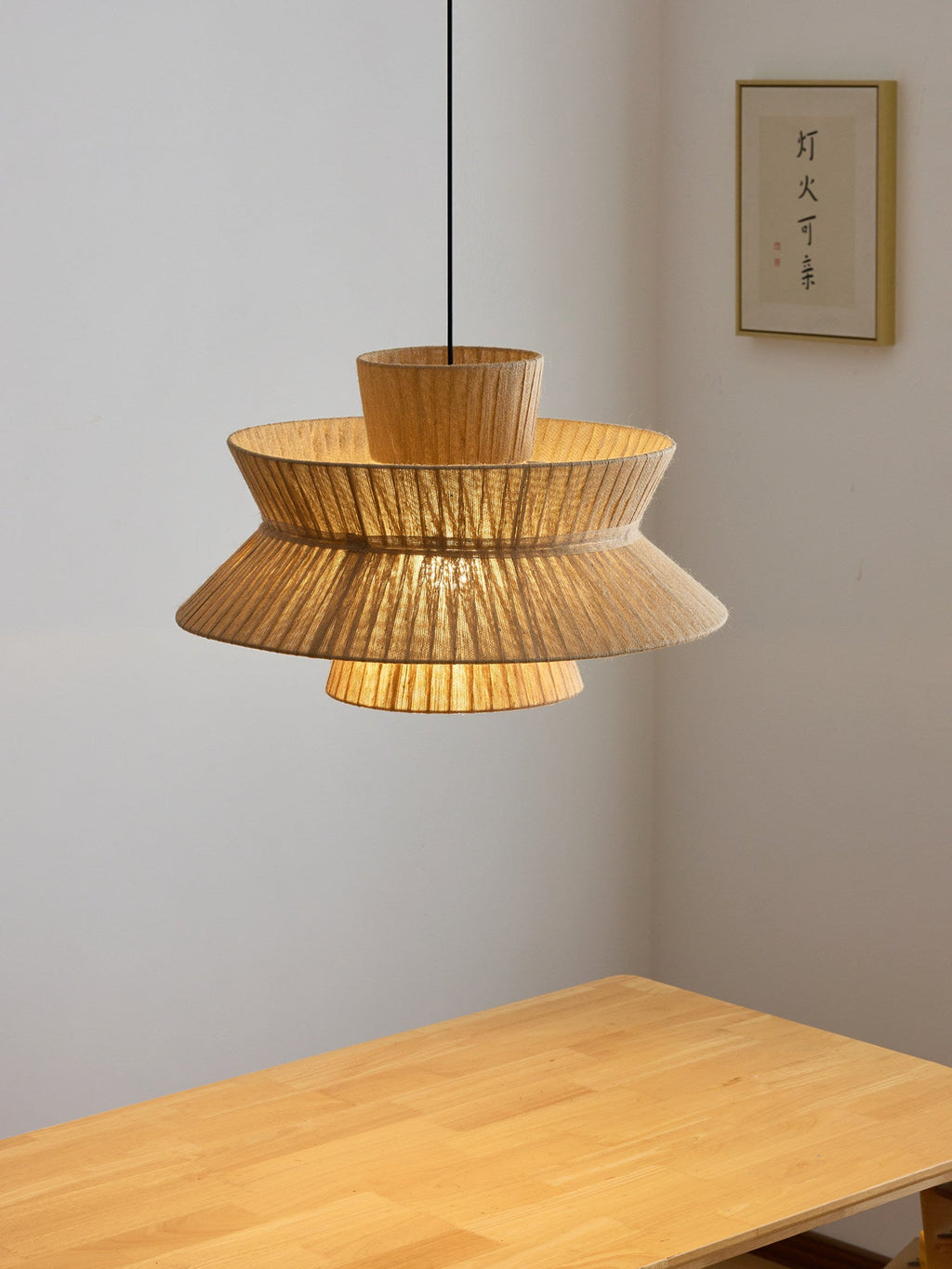 Above a pale wood table in a plain room, this Clérachic pendant flares from a narrow cap to a wide pleated skirt.