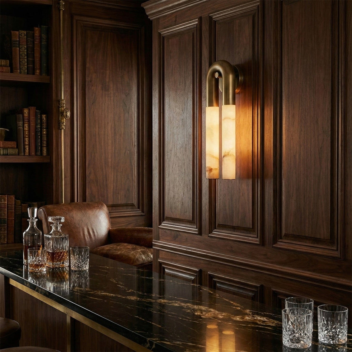 Bronze Arch wall sconce glowing on a dark walnut-panelled wall above a dark stone bar with crystal decanters