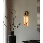 Bronze Arch wall sconce lit on a pale grey wall beside a black vase of bare branches