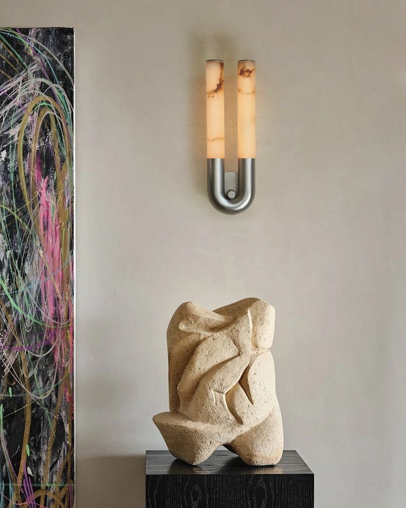 Nickel Arch wall sconce lit above a carved stone sculpture beside a brightly painted canvas