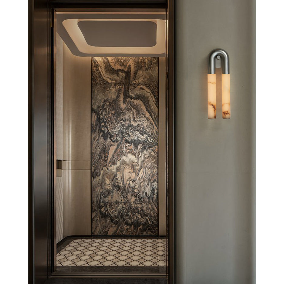 Nickel Arch wall sconce hung arch-up beside a doorway lined with veined marble