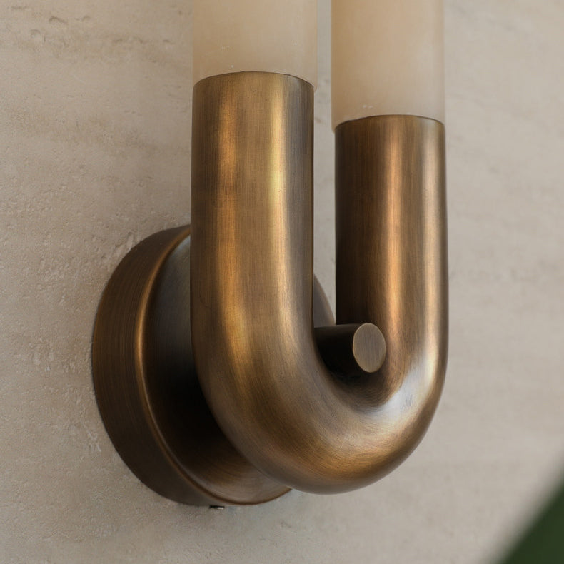 Close-up of the bronze U-bend and round wall plate holding the two alabaster tubes, hung arch-down