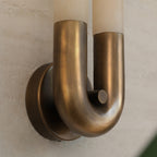 Close-up of the bronze U-bend and round wall plate holding the two alabaster tubes, hung arch-down