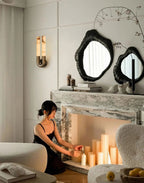 Bronze Arch wall sconce on a panelled living room wall beside a marble fireplace lit with candles