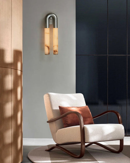 Nickel Arch sconce hung arch-up on a grey wall above a cream boucle armchair by a dark window