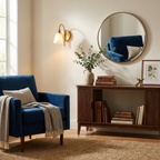 Next to a round mirror and a navy blue armchair, this Clérachic sconce's brass arm angles its light downward.