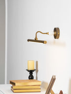 This Clérachic wall sconce in bronze glows above a table with a candle and stacked books, its curved arm visible from the side.