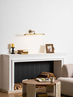 This Clérachic wall sconce in bronze glows above a mantel with a candlestick, stacked books and a framed photo.