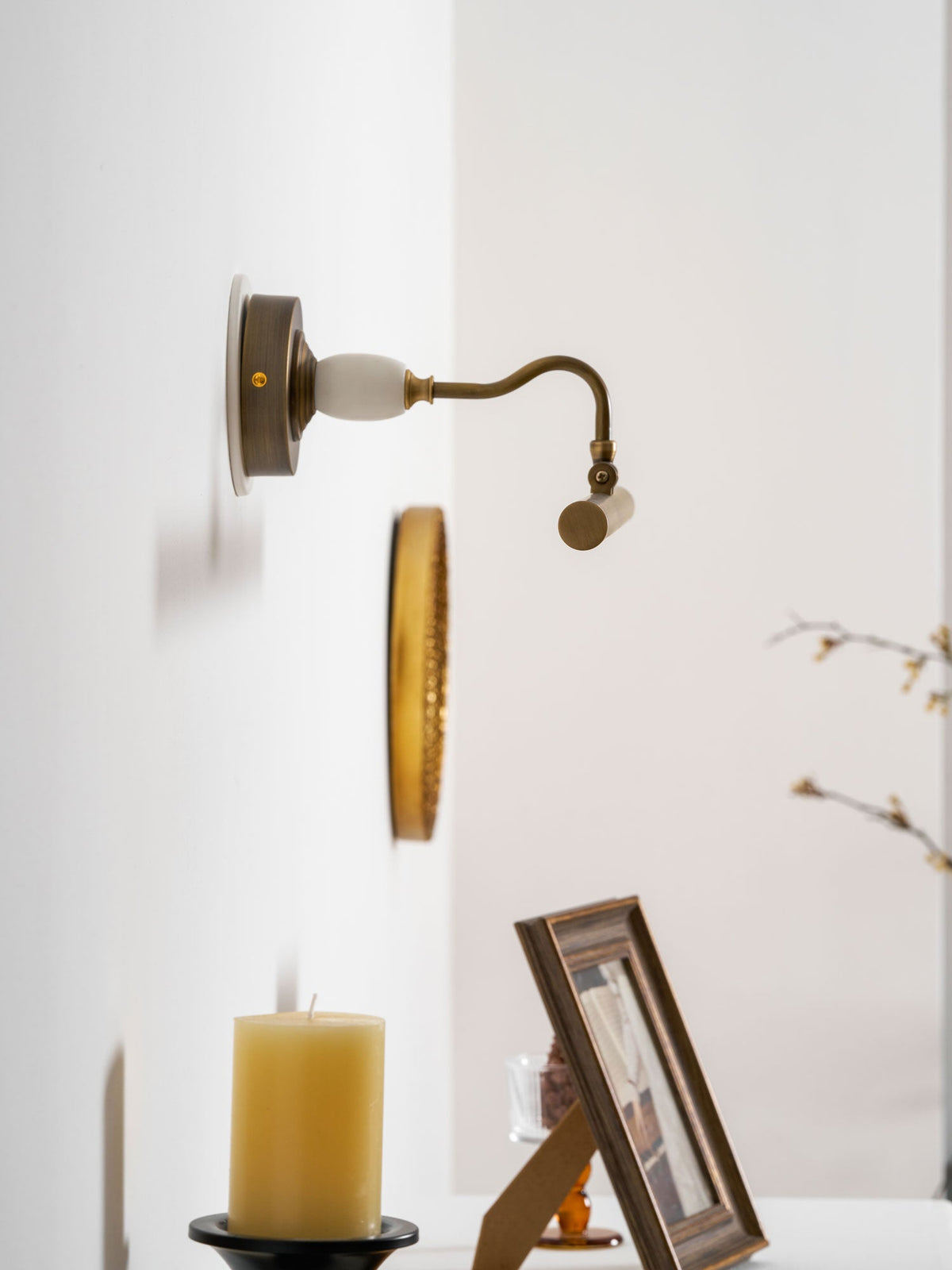 Mounted in a corner, this Clérachic wall sconce in bronze glows above a candle and a framed photo on a round table.