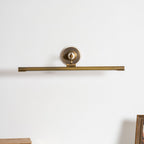 This Clérachic wall sconce in bronze sits unlit against a plain background, with a wooden frame edge in the corner.