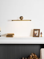 Near a dark fireplace surround, a white mantel with stacked books and a framed photo glows under this gold Clérachic wall sconce.