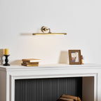 Viewed at an angle, this Clérachic wall sconce in gold lights a mantel with a candle, books and a framed photo.