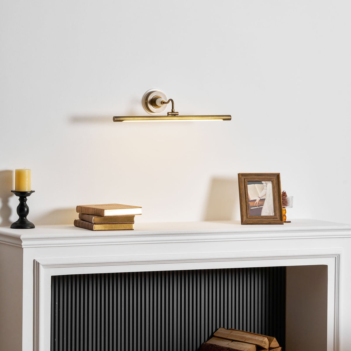 Viewed at an angle, this Clérachic wall sconce in gold lights a mantel with a candle, books and a framed photo.