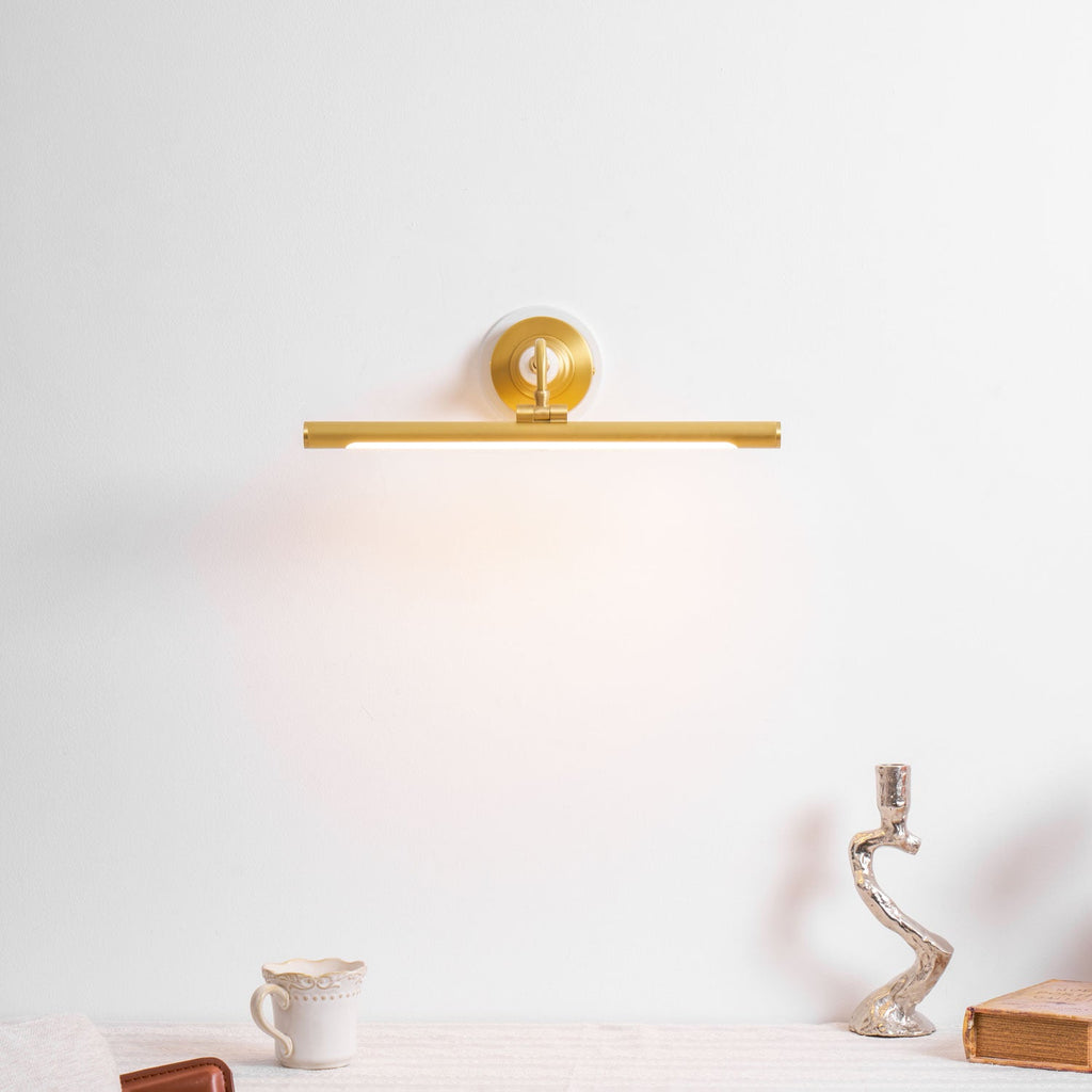 This Clérachic wall sconce in gold glows softly above a table set with a small jug and an ornate candlestick.