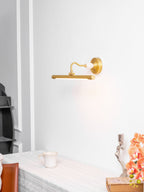 A curved gold mounting arm on this Clérachic wall sconce sits above a table with a candlestick, jug and orchid, in a softly lit setting.