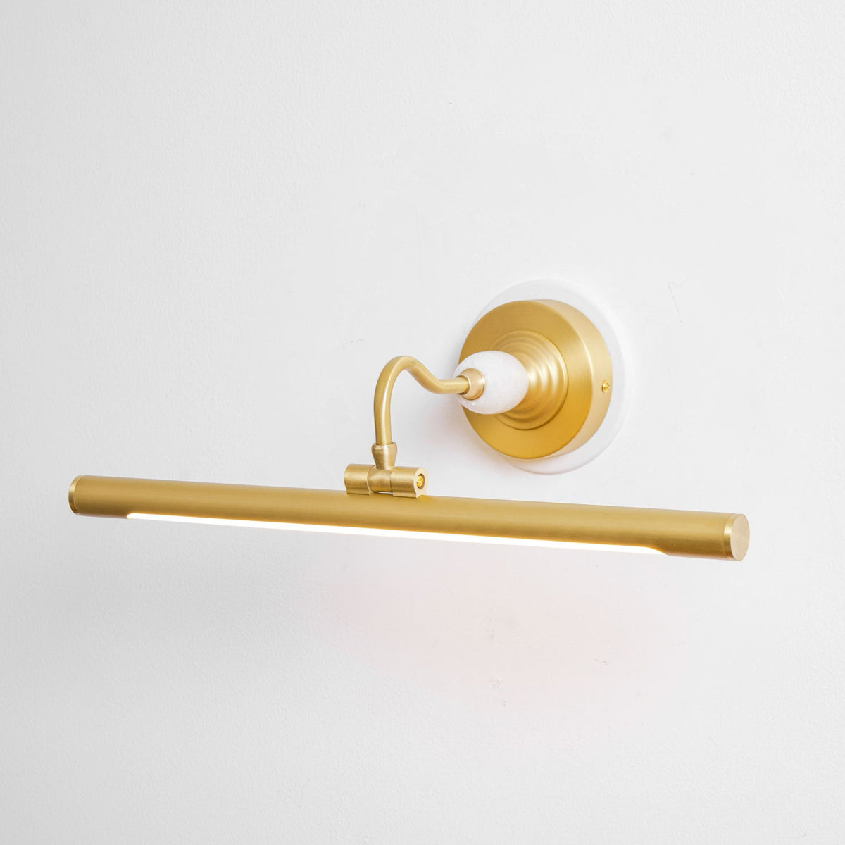 Close view of this Clérachic wall sconce in gold, glowing softly with its curved arm and round wall plate visible from the front.
