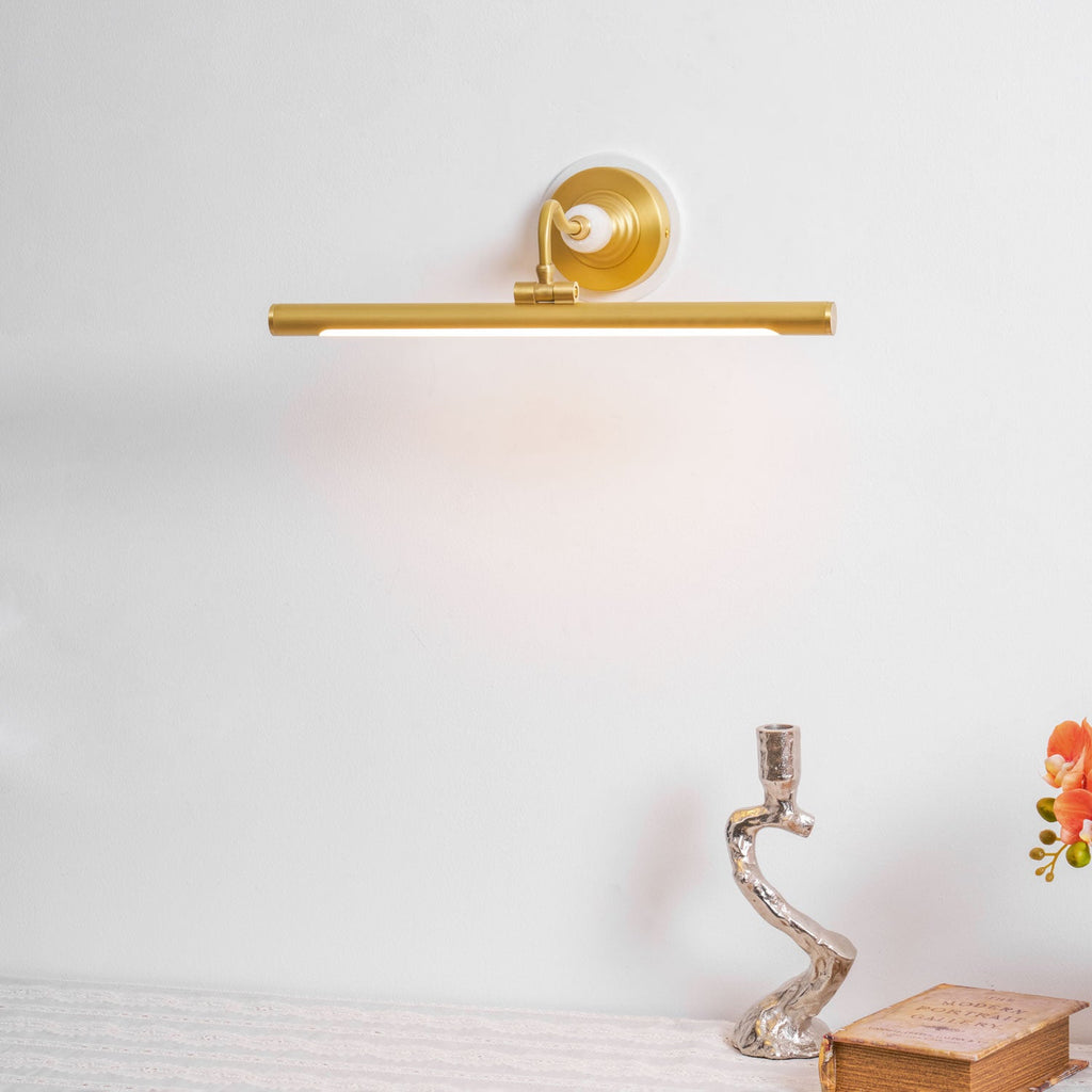 Lit against a plain wall, this Clérachic wall sconce in gold sits above a styled tablescape with a candlestick and open book.